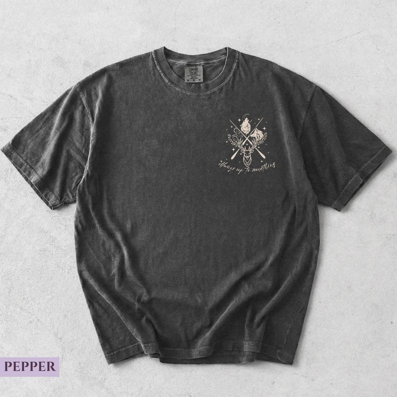 May include: A dark gray t-shirt with a graphic of a deer, wolf, and crossed oars, with the text "Always up to something." The shirt is flat lay