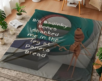 Può includere: Una grande coperta rettangolare con un'illustrazione di un personaggio dei cartoni animati e il testo "Big Badinky Bones shanked me in the leg at Panera Bread". La coperta ha una combinazione di colori verde acqua, grigio e bianco.