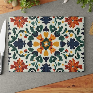 May include: A white cutting board with a colorful floral pattern. The pattern features blue, green, orange, and yellow flowers and leaves. The board is made of tempered glass and is heat resistant.