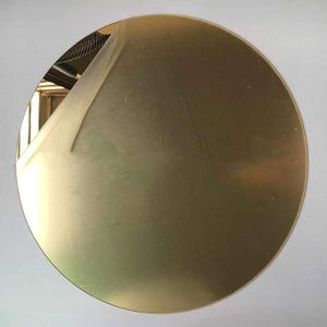 May include: A large, round, gold-colored metal disc. A protective film is partially peeled back from the top left edge, revealing a shiny surface. The disc is set against a plain white background.