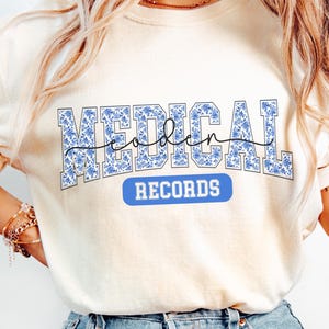 May include: A white t-shirt with a blue and white patterned graphic that says "Medical Records" in a varsity style font.