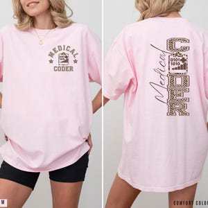 May include: A light pink t-shirt with the words "MEDICAL CODER" printed on the front and back. The front design includes a star and a graphic. The back design features the word "CODER" in a leopard print.