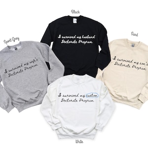 May include: A collection of sweatshirts in various colors: sport grey, black, sand, and white. Each sweatshirt features the phrase "I survived my" followed by a family member's relationship to the program, or "custom" and "Doctorate Program" in a script font.