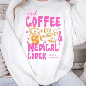 May include: White sweatshirt with the text "iced COFFEE & MEDICAL CODER all day every day" in pink and orange. The design includes an iced coffee, computer, stethoscope, and books.