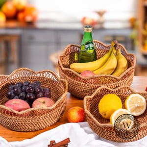 Może przedstawiać: Trzy wiklinowe kosze z falbankami, wypełnione owocami. Kosze są brązowe i naturalne. Owoce to winogrona, jabłka, banany, cytryny i limonki. W tle znajduje się butelka wody Perrier.