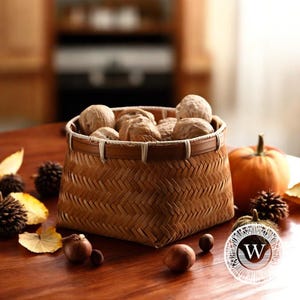 Könnte beinhalten: Ein geflochtener Bambuskorb mit weißem Rand, gefüllt mit Walnüssen, steht auf einem Holztisch mit Herbstdekoration.