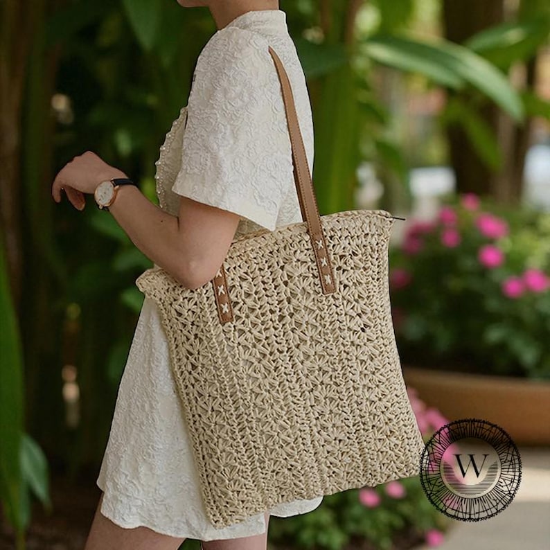 Puede incluir: Un bolso tote tejido beige con correas de cuero marr&oacute;n. El bolso tiene forma rectangular y cierre de cremallera. Las correas est&aacute;n unidas con costuras decorativas. El bolso se lleva al hombro.