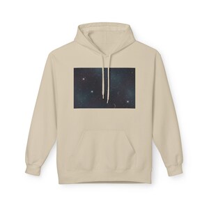 May include: A beige hooded sweatshirt with a front pocket. The front panel displays a rectangular image of a night sky with stars and a crescent moon. The hoodie is a neutral colour.