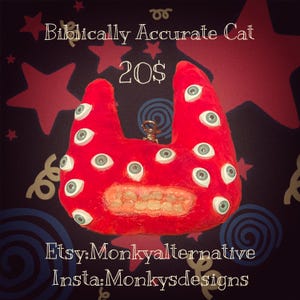 May include: A red plush cat-shaped creature with multiple eyes and a mouth full of teeth. The text "Biblically Accurate Cat" and "20$" are displayed at the top. The Etsy shop name "Monkyalternative" and Instagram handle "Monkysdesigns" are at the bottom.