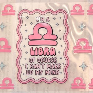 May include: A sheet of stickers featuring three large rectangular labels with scalloped edges, each displaying the pink Libra zodiac symbol, the text I'M A LIBRA OF COURSE I CAN'T MAKE UP MY MIND, and small stars, surrounded by several smaller Libra icons.