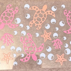 May include: A clear transfer sheet featuring a repeating pattern of sea turtles, starfish, coral branches, and circular bubbles in shades of pink and peach. The design elements are arranged across the transparent surface for application.