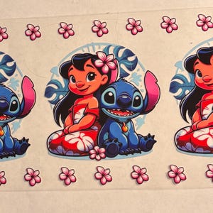 May include: A clear transfer sheet featuring three identical graphic prints of a girl with long black hair and a pink flower in her hair sitting next to a blue alien character. Both are surrounded by tropical leaves and pink hibiscus flowers.