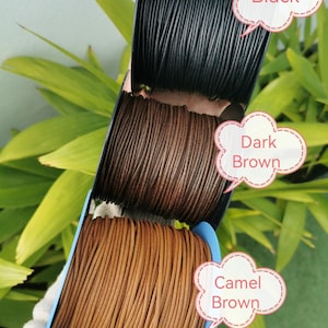 A hand holding a spool of leather cord in three different colors: black, brown, and camel brown. The cord is arranged in a row, with each color represented by a speech bubble above it.