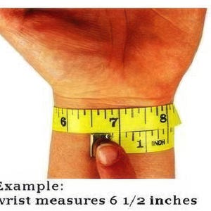 A person's wrist is being measured with a yellow measuring tape, which is wrapped around the wrist and displaying the measurements in inches.