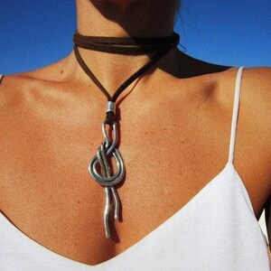 A woman wearing a white tank top and a silver necklace with a large knot pendant.