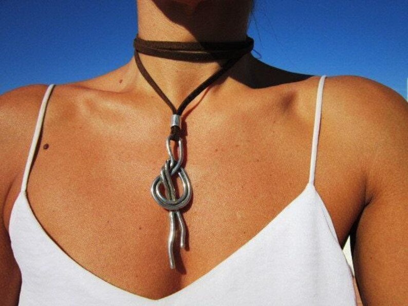 A woman wearing a white tank top and a silver necklace with a large knot pendant.