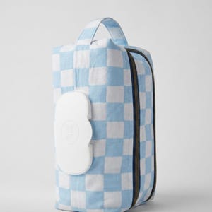 May include: A rectangular fabric pouch featuring a light blue and white checkered pattern. The pouch includes a top handle, a dark zipper closure along the side, and a white plastic flip-top dispenser lid centered on the front panel.
