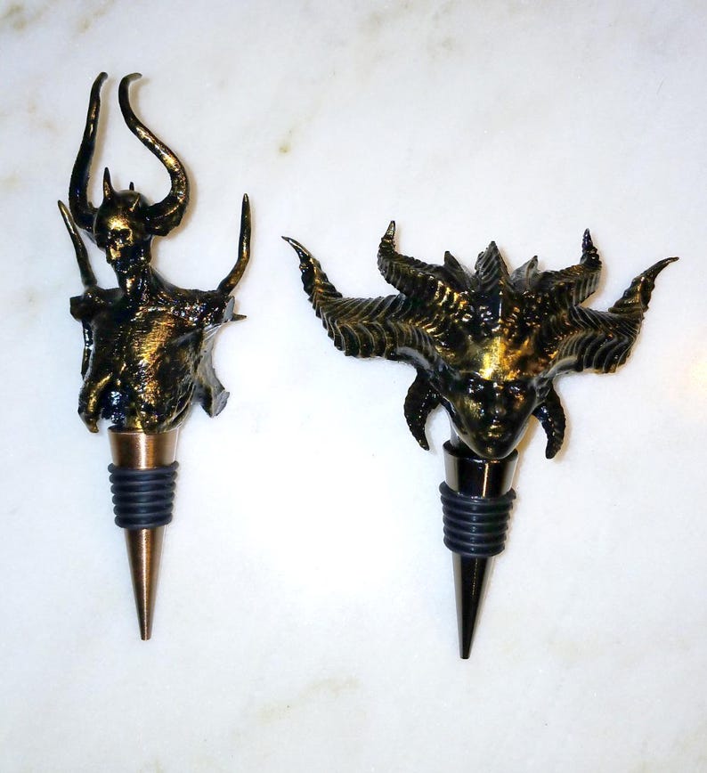 May include: Two gold-coloured bottle stoppers shaped like demonic figures. The stoppers are made of a textured material and have a black rubber base.