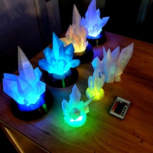 May include: A set of six crystal-shaped lamps with different colored lights. The lamps are on a wooden table and are controlled by a remote control.