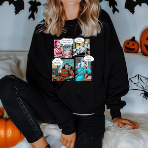 May include: Black sweatshirt featuring a four-panel comic strip with Halloween horror characters. The panels include Jason Voorhees, Pennywise, Freddy Krueger, and Michael Myers, each with speech bubbles. The text in the speech bubbles reads "Did you see how I chased them?", "Very Demure", "Very Mindful", and "Very Scary".