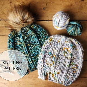 May include: Two knitted hats with a fuzzy pom pom on top. The hats are made with a chunky yarn in shades of blue, green, and white. The yarn has a speckled effect. The hats are lying on a wooden surface with two balls of yarn.