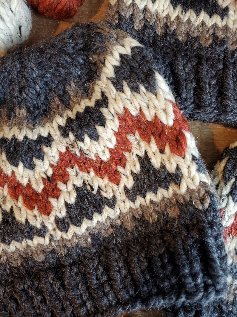 May include: A close-up of a knitted hat with a black, white, brown, and red geometric pattern. The hat is made of wool and has a soft, fuzzy texture.