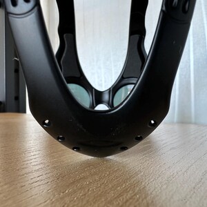 May include: A close-up shot of a black, curved object with multiple holes and rounded edges. The object has a matte finish and appears to be made of a sturdy material. The design includes two oval-shaped cutouts on each side.