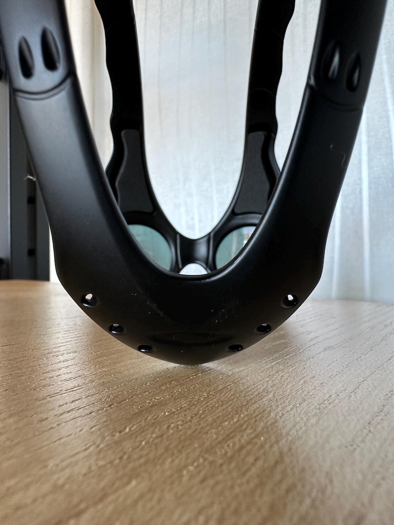 May include: A close-up shot of a black, curved object with multiple holes and rounded edges. The object has a matte finish and appears to be made of a sturdy material. The design includes two oval-shaped cutouts on each side.