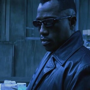 May include: A man wearing black-framed glasses and a black leather jacket. The image is a close-up shot with a blue-toned colour scheme. The man has short, dark hair and a serious expression.