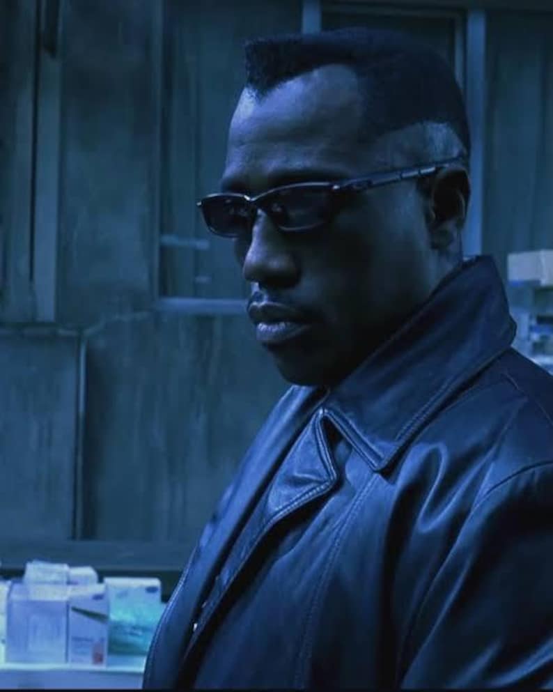 May include: A man wearing black-framed glasses and a black leather jacket. The image is a close-up shot with a blue-toned colour scheme. The man has short, dark hair and a serious expression.