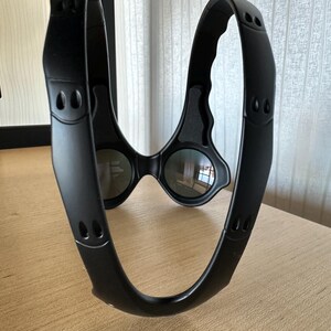 May include: Black sports eyewear with a unique, wraparound design. The glasses feature dark lenses and a thick, curved frame with small, decorative cutouts. The frame appears to be made of a matte material.