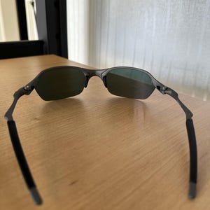 Pu&ograve; includere: Occhiali da sole grigio scuro con lenti verdi. Gli occhiali da sole hanno un design elegante e moderno con una montatura sottile e aste curve. Le lenti sono di colore verde scuro.