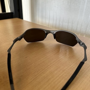 Pode incluir: &Oacute;culos de sol cinza escuro com um design semi-sem aro. As lentes s&atilde;o de cor marrom escuro e as arma&ccedil;&otilde;es s&atilde;o cinza fosco. As hastes t&ecirc;m um revestimento de borracha preta para conforto.