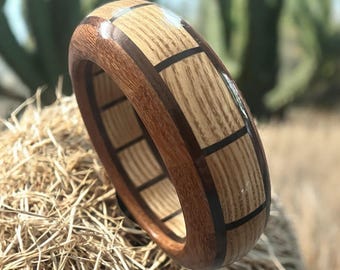 May include: A thick wooden bangle bracelet featuring a segmented design with alternating light tan oak and dark brown wood panels, separated by thin black inlay lines, creating a smooth, polished, and rounded circular band.