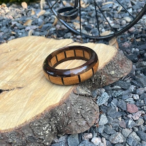May include: A handcrafted wooden bracelet with a dark brown and light brown segmented design. The bracelet is displayed on a natural wood slice, showcasing the contrasting wood tones and craftsmanship. The bracelet's diameter is approximately 7 cm.