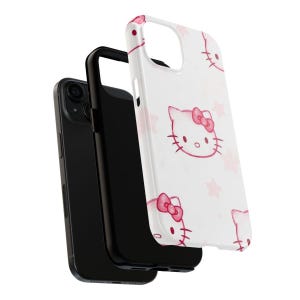 May include: A white phone case with a repeating pattern of pink Hello Kitty faces and stars. The case is displayed with a black phone and a black phone case.