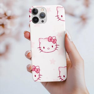 May include: A white phone case with a repeating pattern of pink Hello Kitty faces and bows, and pink stars. The case has a glossy finish and a camera cutout.