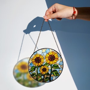 a hand holding a stained glass sunflower hanging from a chain