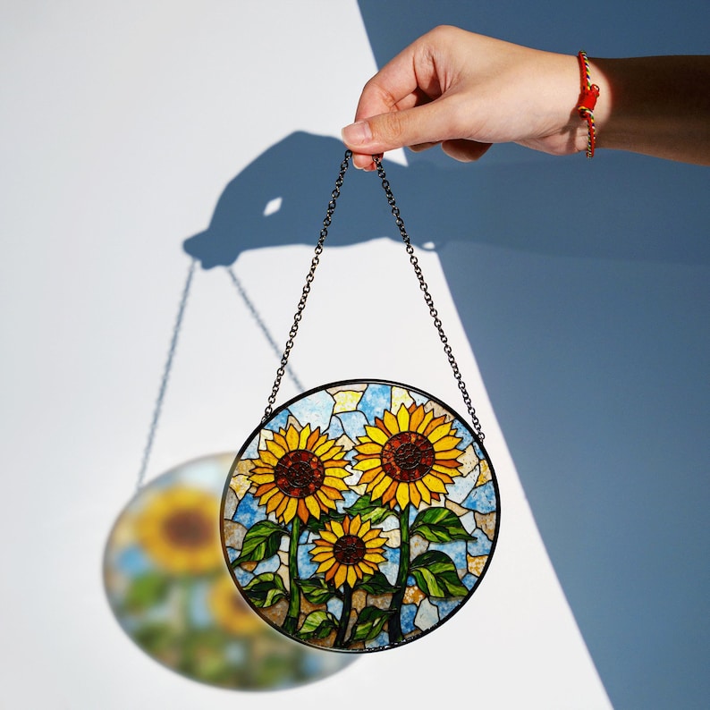 a hand holding a stained glass sunflower hanging from a chain