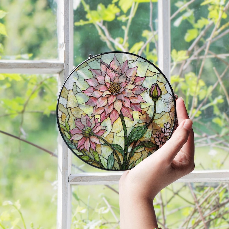 a hand holding a stained glass flower in front of a window