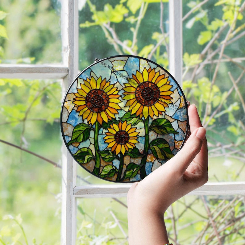a hand holding a stained glass sunflower in front of a window