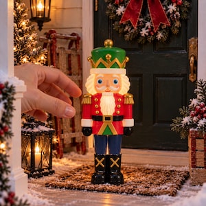 May include: A light-up nutcracker figurine featuring a green hat, red jacket with gold accents, white beard, and black boots. The figure has a glowing torso and face, standing upright with a classic soldier uniform design and painted facial features.