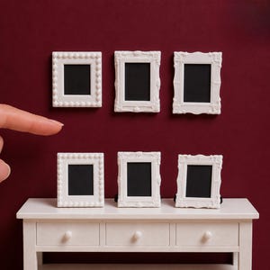 Può includere: Sei cornici portafoto bianche in miniatura con centri neri disposte su due file. La fila superiore presenta tre cornici con diverse texture dei bordi, mentre la fila inferiore mostra tre cornici abbinate su un tavolo console bianco con tre cassetti.