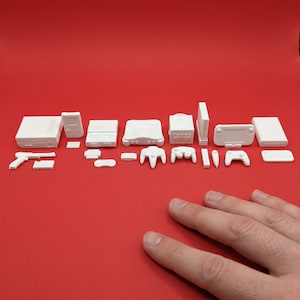 Puede incluir: Una colección de miniaturas blancas de consolas y mandos de videojuegos, incluyendo una consola portátil, un mando de Nintendo 64 y una consola Switch, dispuestas sobre una superficie roja.