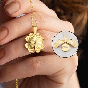 May include: A gold necklace with a four-leaf clover pendant. The pendant opens to reveal a small, round space inside.