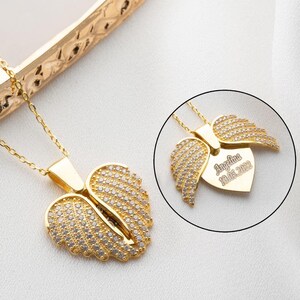 May include: Gold necklace with a heart-shaped pendant featuring two angel wings with clear cubic zirconia stones. The pendant has an inscription that reads "Angelina 01.01.2022".