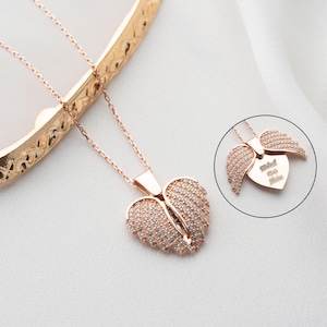 May include: A rose gold necklace with a heart-shaped pendant featuring two angel wings. The pendant is adorned with clear cubic zirconia stones. The back of the pendant has the inscription "With Love Always".