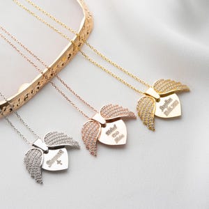 May include: Three silver necklaces with angel wing pendants. Each pendant features a heart-shaped charm with a name and date engraved on it. The names are "Michael", "Sophia", and "Angelina Marie 2021".