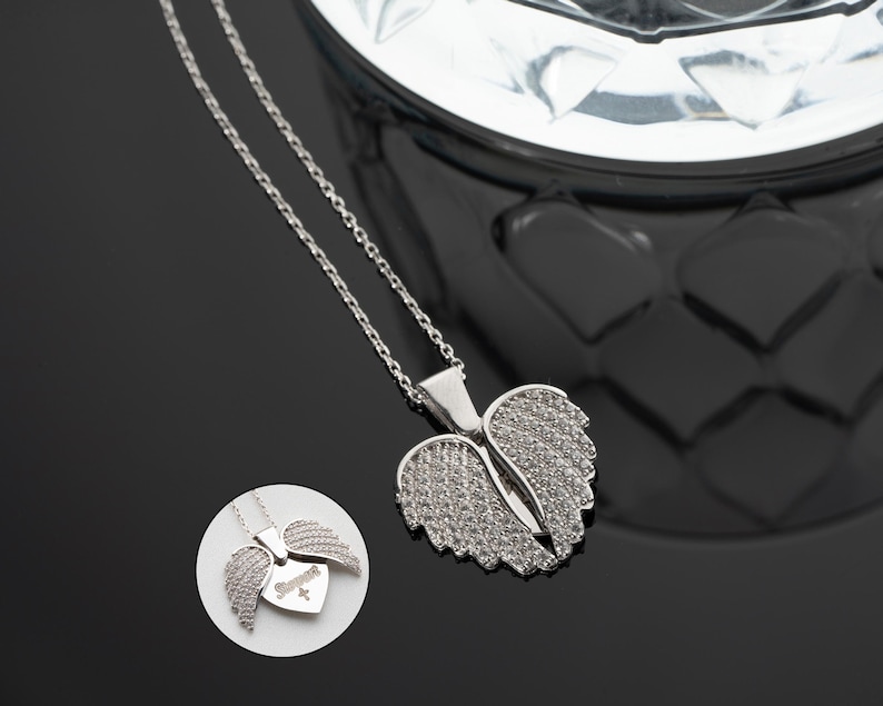 May include: Silver necklace with a heart-shaped pendant featuring angel wings adorned with sparkling cubic zirconia stones.