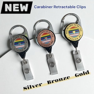 May include: Three carabiner retractable clips with the text "YOU'RE SAFE TO BE AROUND ME". The clips are silver, bronze, and gold. Each clip has a rainbow heart design.